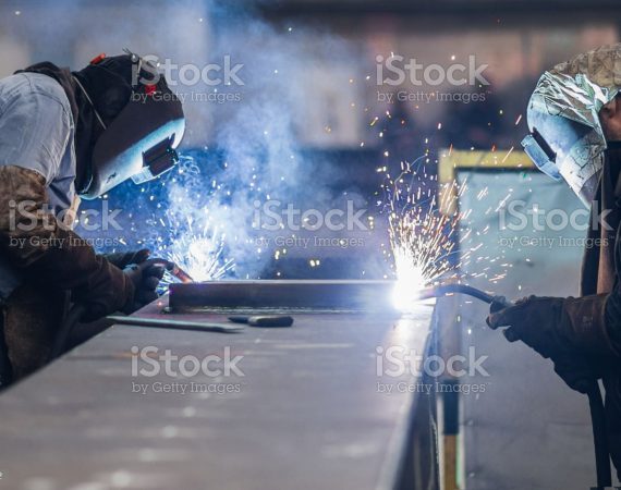 Men using welding torch to cut metal sheet in workshop.